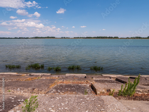Konstfotografi Modified bank of the Danube River at Čunovo with concrete slope protection, calm water and a wide blue summer sky in southwestern Slovakia