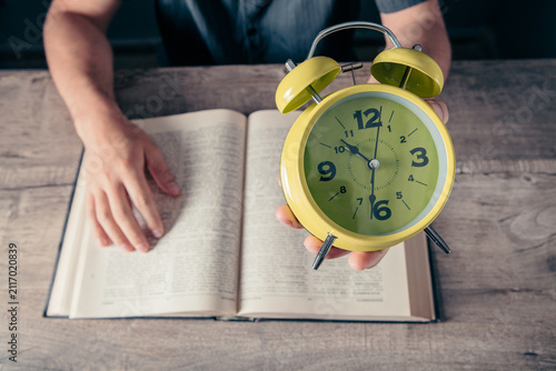 Man holding alarm clock and reading a book. Time management concept.