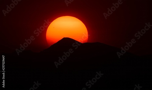 an eerie sunset of the sun sinking behind the front range of the colorado rocky mountains, through the smoke of the western forest fires , as seen from broomfield