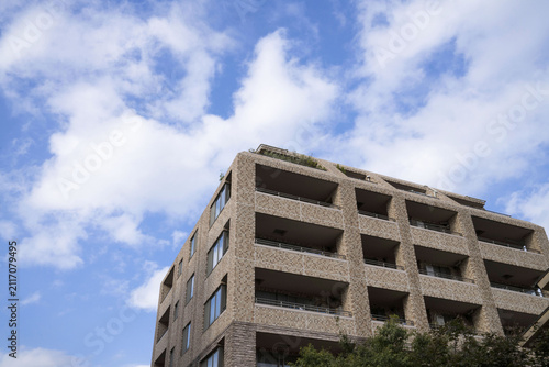 Naklejka 青空と白い雲を背景にそびえ立つブラウンのタイル張りが美しいマンション外観