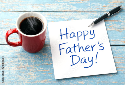 Happy fathers day greeting card with steaming coffee mug and pen on wooden table