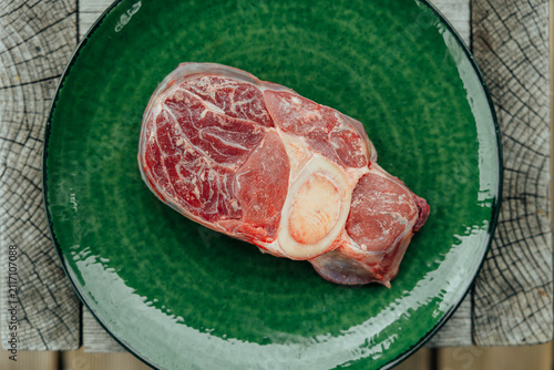 Canvas Print Close-up of a raw cross-cut beef shank with visible marrow bone and muscle tissue on a glossy green plate