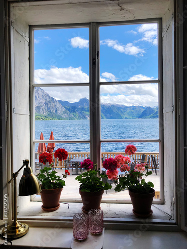 View to Lake Traunsee and alpine mountains through window with red Potted Geraniums , Upper Austria