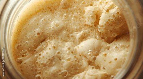 Overhead close-up of bubbly active sourdough starter fermenting inside a glass jar