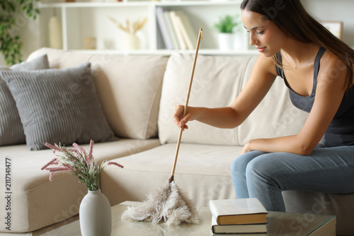 фотографія Happy woman cleaning coffee table with a feather duster