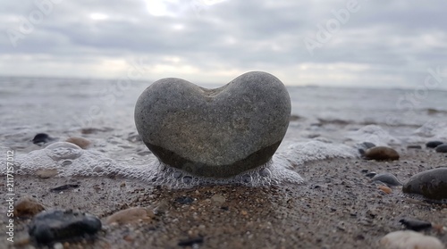 Heart-shaped pebble on a sandy shore with incoming ocean waves under a cloudy sky, symbolizing love, peace, and natural coastal beauty outdoors
