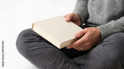 Person sitting cross-legged while holding a blank hardcover book with copy space on a clean white background for creative design projects