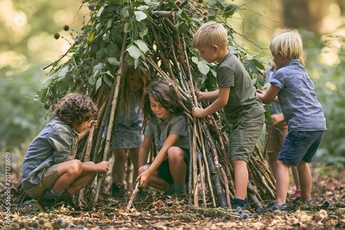 children building imaginative nature forts with sticks, leaves and branches in a peaceful woodland, curiosity, teamwork, outdoor exploration, soft morning light
