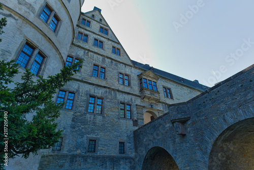An exterior view of Wewelsburg Castle in Westphalia, Germany, highlighting its historic stone architecture with a round tower, gabled building, and a connecting stone bridge under a clear sky.
