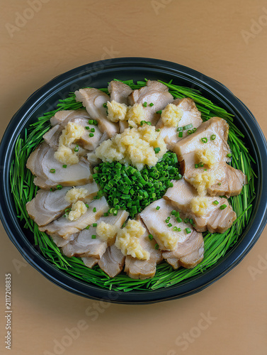 Overhead shot of delicious sliced pork belly with garnish on a black plate