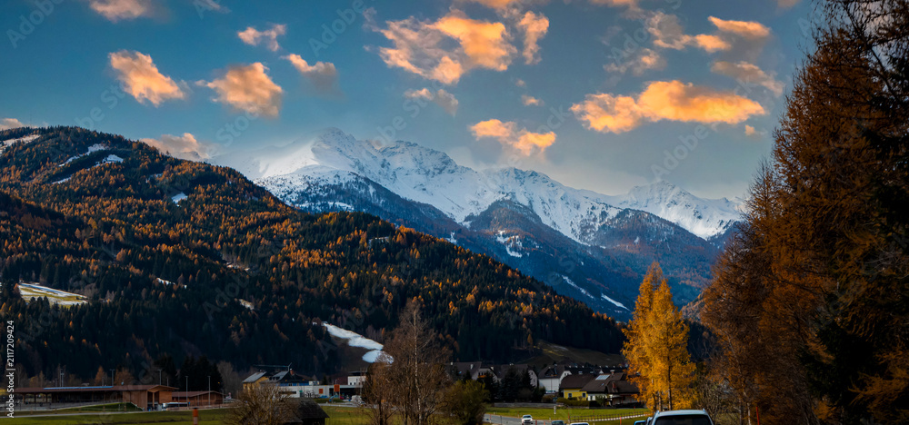 Fototapeta premium The scenic mountain road in alpine countryside with colorful autumn trees and snow capped peaks with wet asphalt road winding through autumn forest to hallstatt austria at sunset