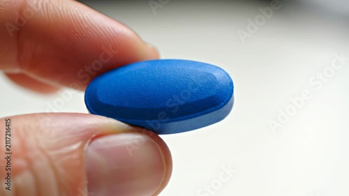 A person holds a small blue medicinal tablet between their fingers to demonstrate proper administration of prescription drugs for healing common ailments within a healthcare or pharmacy