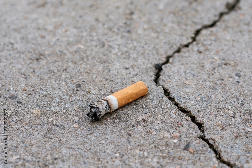Obraz premium The cigarette butt on cracked pavement in desolate urban street scene