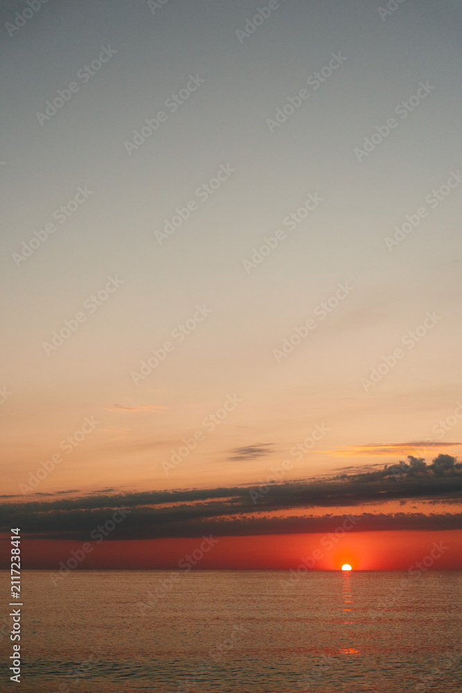 Obraz premium Calm sunset over a tranquil sea paints warm orange light across the water and horizon, inviting reflection and peaceful mood.
