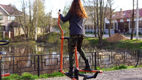 A girl exercises on an outdoor exercise machine.
