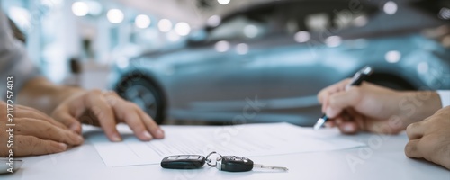 Close-up of hands signing a car purchase contract with keys on a table. Ultra-realistic dealership scene highlights auto buying and vehicle ownership transfer.