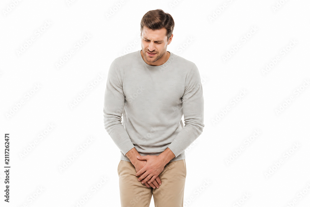 Obraz premium A man in a light grey sweater and tan pants is holding his lower back, suggesting discomfort or pain.