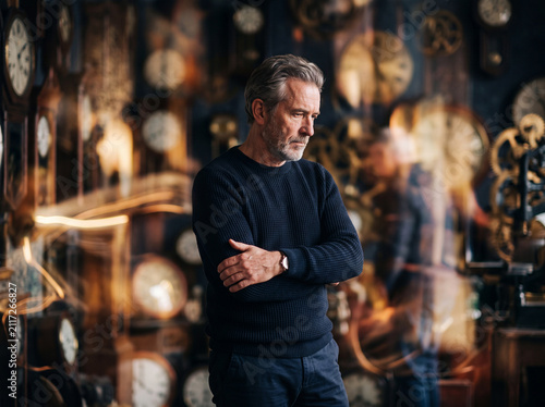 Male menopause and andropause theme with thoughtful mature man standing in front of clock background