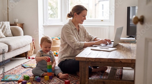 Authentic shot of professional mother working on laptop from home while toddler child plays nearby