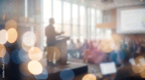 Business presenter standing on stage in front of blurred audience in bright modern office conference hall with bokeh lighting for professional corporate event photography
