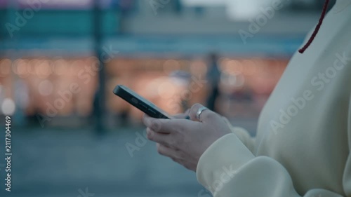 Close up of woman's hands using smartphone outdoors at night in city