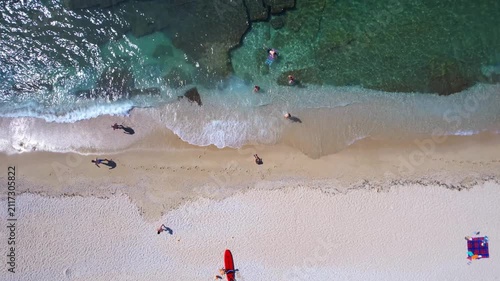 Aerial drone of a peaceful beach in Thassos, Greece, featuring transparent turquoise water, paddleboards, swimmers and a beautiful Mediterranean coastline.
