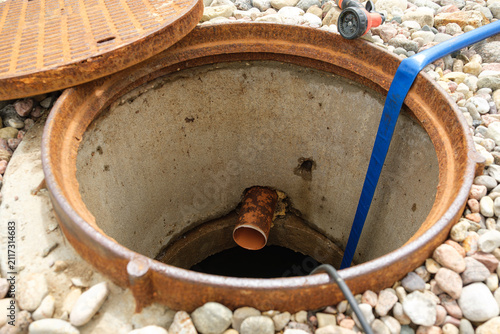 An open sewer manhole. A service cleaning of blocked sewer. A concrete septic tank with a plastic pipe. Rinse and pumping water out. Maintenance work, utility service, underground infrastructure.