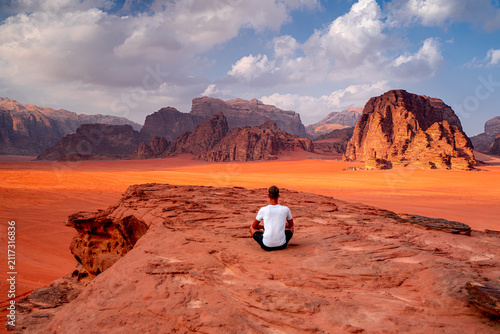 Bild auf Leinwand Man sitting on rock looks out at desert horizon with mountains, Wadi Rum, Jordan