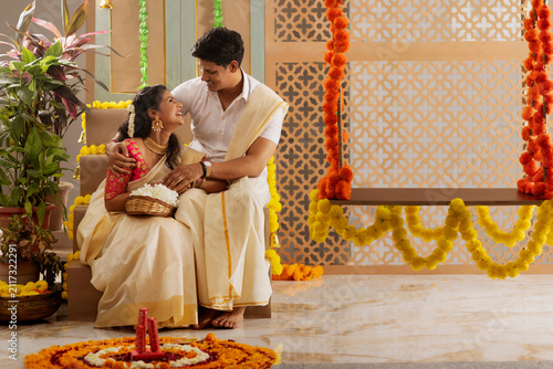 South Indian couple decorating house with flower garland to celebrate Onam