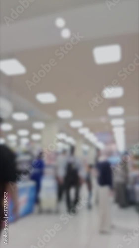 Blurred, out-of-focus vertical video of people walking in a supermarket background with bokeh lighting.