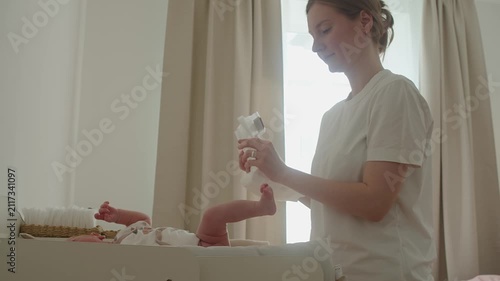 Mother opens clean diaper and arranges it before dressing baby on changing table. Preparation remains precise and unhurried, making hygiene routine smoother, safer, and more comfortable for infant.