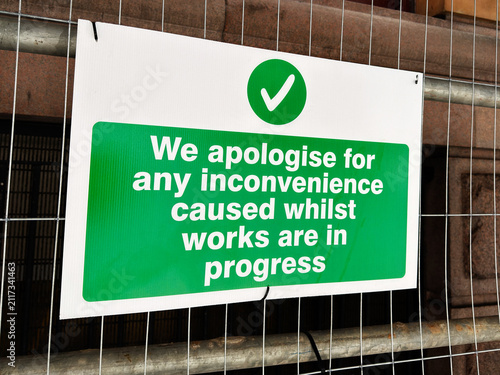 Photography Green apology sign on metal fence apologising for inconvenience while constructi