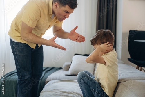 Konstfotografi Adult male in yellow shirt scolding young boy sitting on couch, child covering e