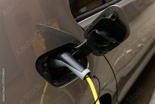 Closeup of an electric car being charged with a yellow power cable plugged into the vehicle charging port