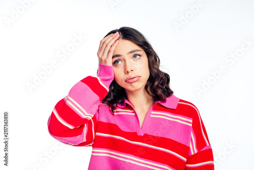 Konstfotografi Young woman in pink striped sweater holds hand to her forehead with a puzzled, f