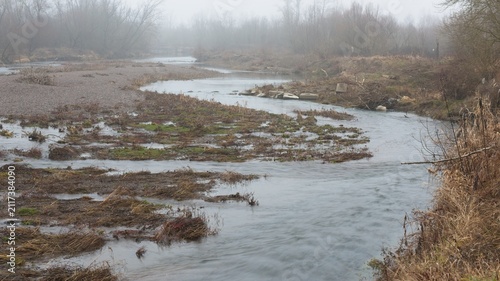 9Winding river flows beneath high riverbank during foggy day