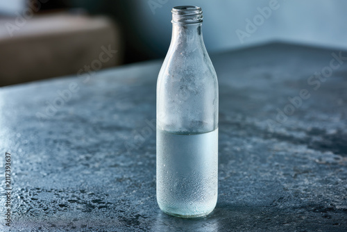 A minimalist, clear glass bottle filled with water rests on a simple, textured table, capturing the essence of clarity and simplicity in a contemporary setting.