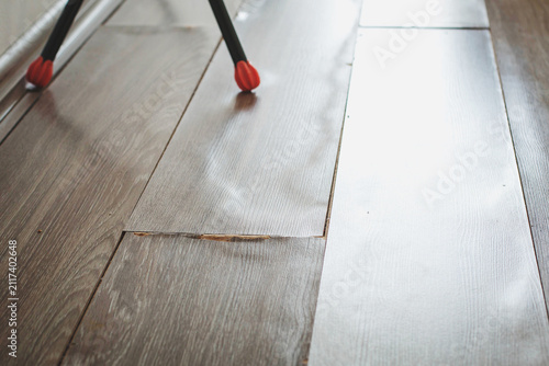 Fotografie Damaged laminate flooring with chipped surface near furniture leg, closeup revea