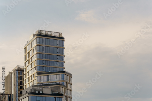 Glass skyscraper corner fragment next to vast cloudy copespace sky. Modern apartment tower top in minimal composition.