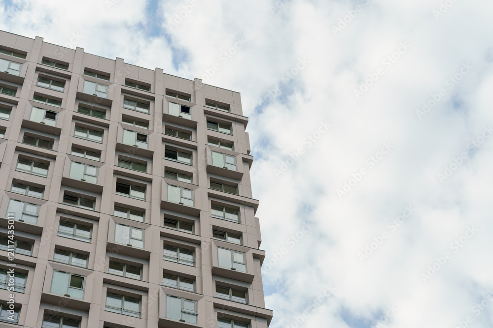 Fototapeta premium Multi story residential building corner with cloudy sky copespace area. Modern apartment block facade fragment in low angle view.