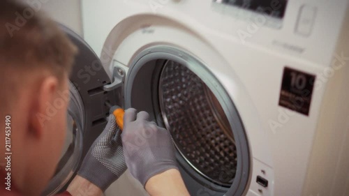 Close-up of gloved hands removing a screw from a washing machine drum in a bathroom. Concept for DIY home appliance repair and saving on technician services