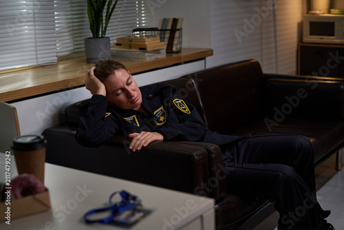 Cuadro en lienzo Caucasian security guard resting on office sofa during break, showing fatigue after shift