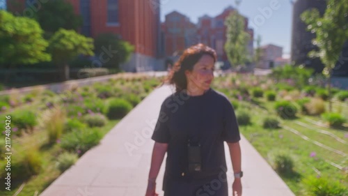 A Woman Strolling Through a Vibrant Urban Park, Carrying a Toy While Enjoying the Sunshine and Breathtaking Landscapes Amidst Striking Architecture