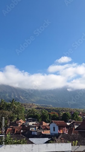 Scenic view of a mountain peak with white clouds, blue sky, and a rural village.