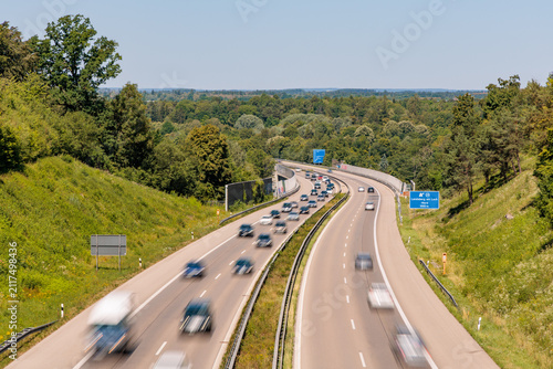 Traffic with blurred cars moving on german Autobahn A96 highway near Landsberg am Lech exit surrounded by green summer trees, high angle view