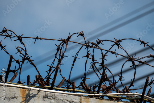 Old and rusty barbed wire usually used for security fences. This wire is made with sharp edges with a blue sky background.