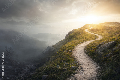 Winding path from foggy valley to sunlit hilltop
