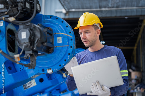 Factory worker wearing safety helmet examining equipment using laptop in contemporary manufacturing environment