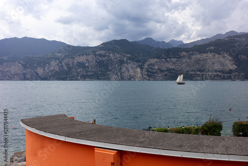 Canvas Print Sailing boat glides across the lake near the mountains in Italy with cloudy sky