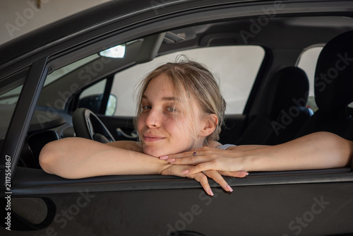Woman sitting in a car with her arms resting on the window smiling at the camera